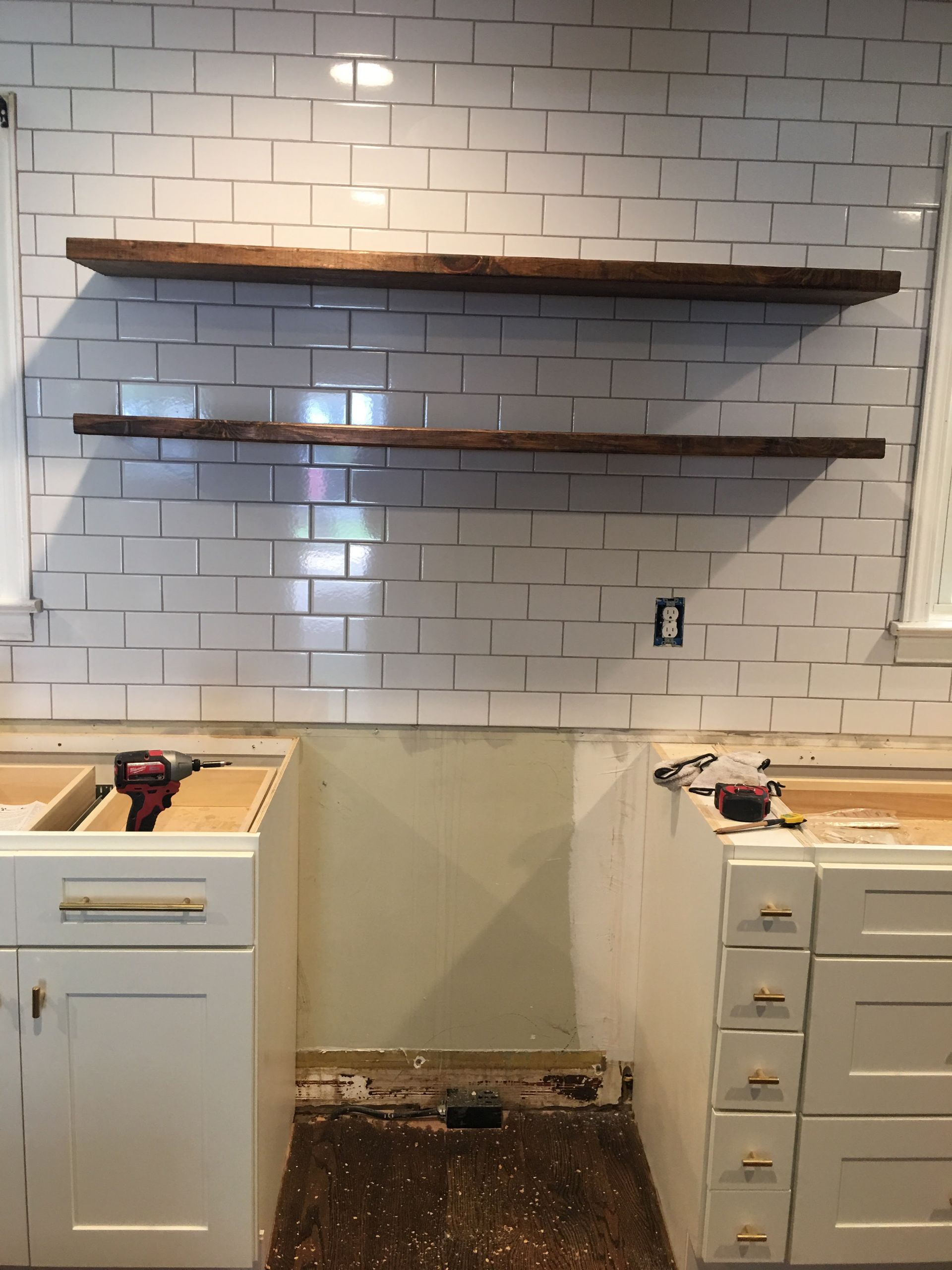 Two wooden shelves on a tiled kitchen wall above white cabinets; construction in progress.