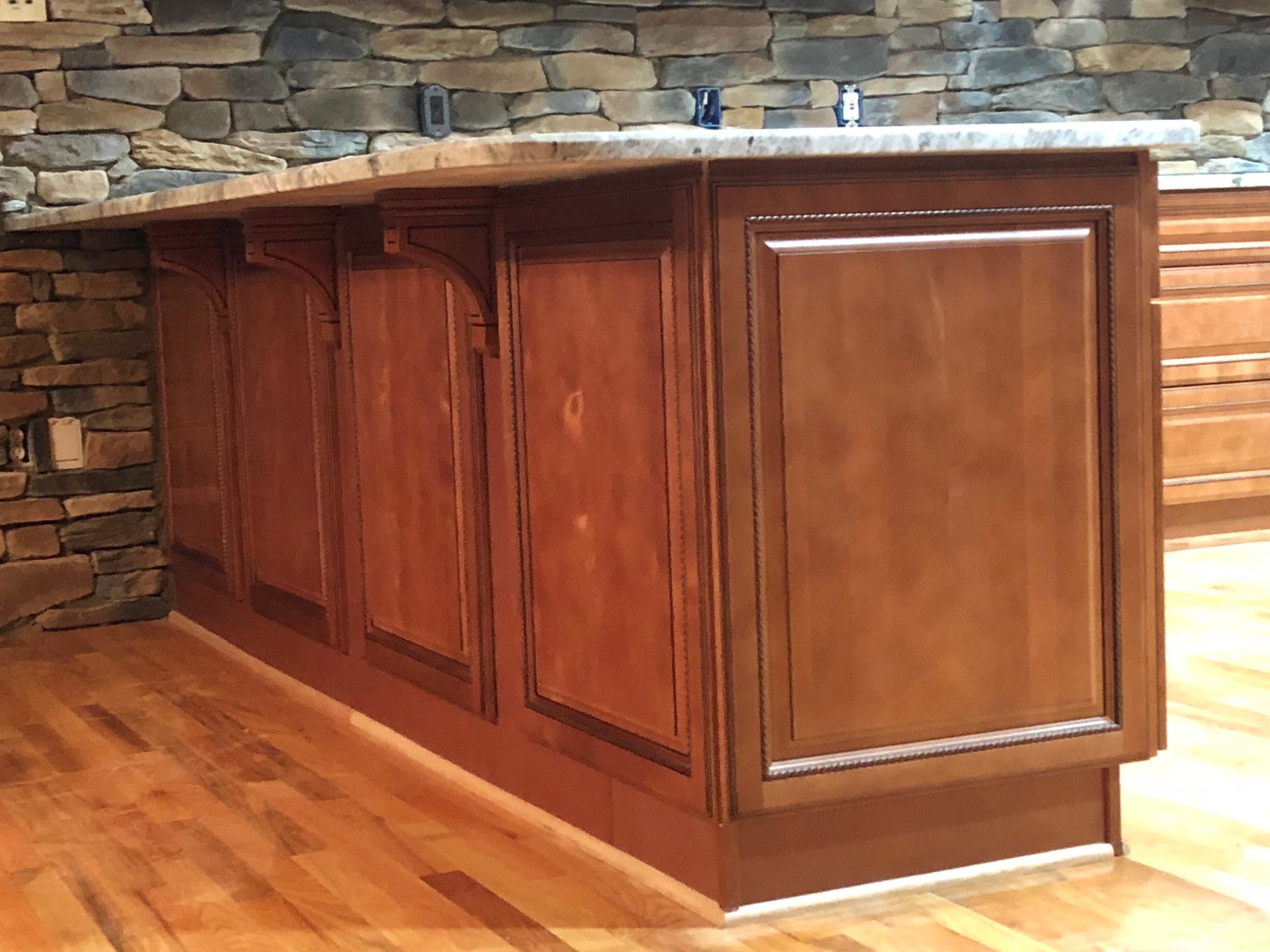Wooden kitchen island with granite countertop, set against a stone wall and hardwood floor.