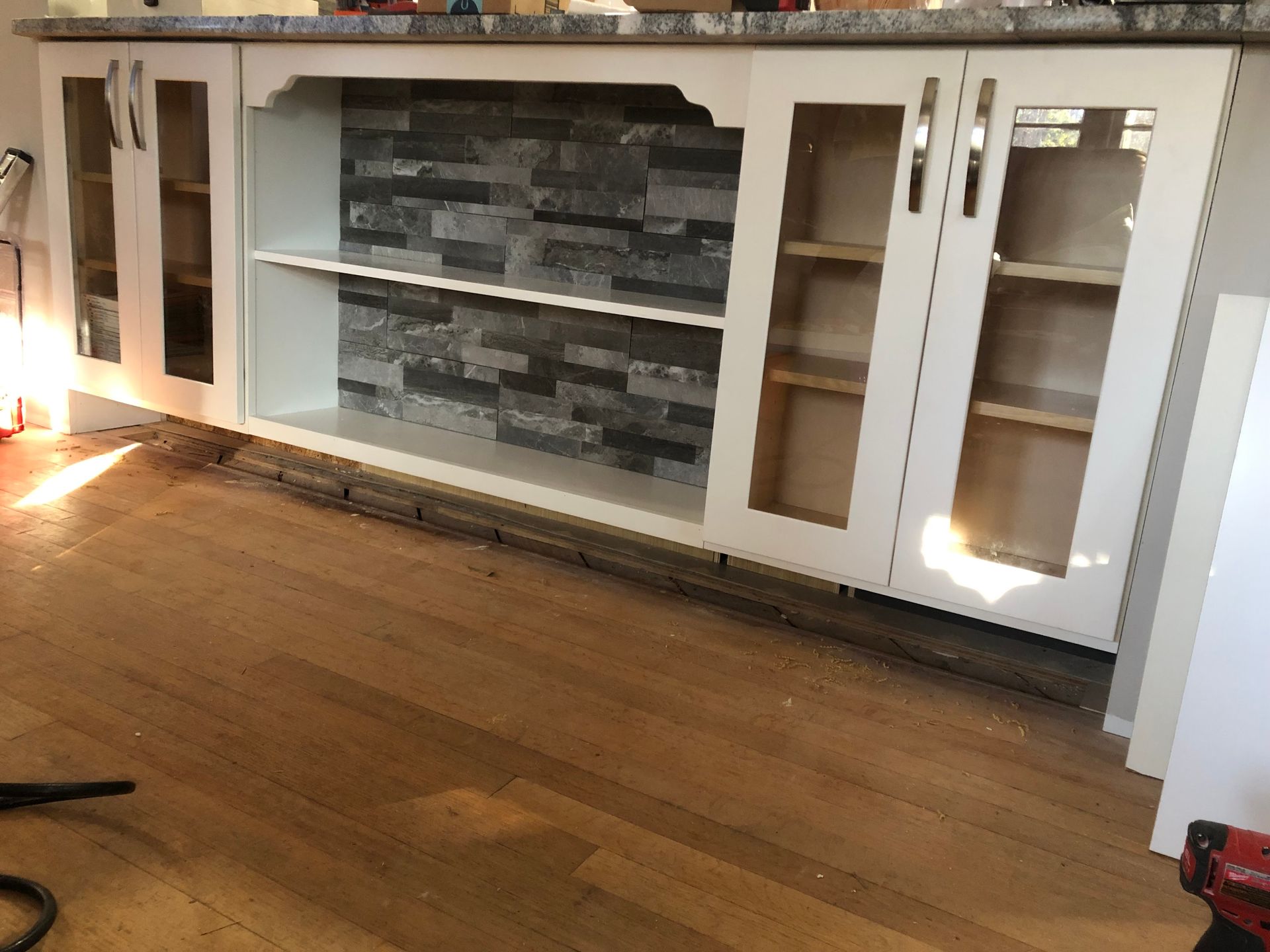 White cabinets with glass doors and a stone backsplash, sitting on a wooden floor.