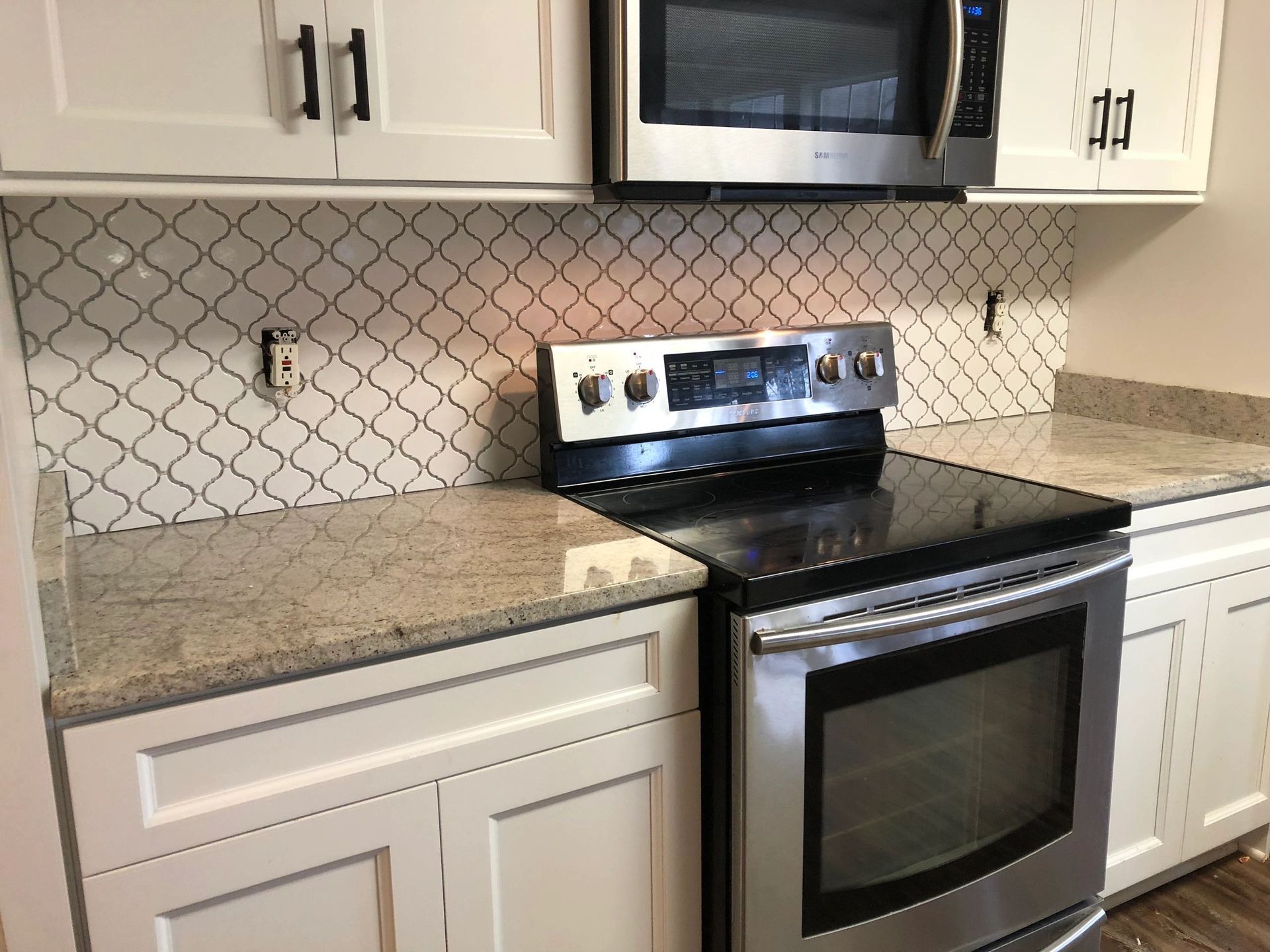 White kitchen with tile backsplash, stainless steel appliances, and granite countertops.