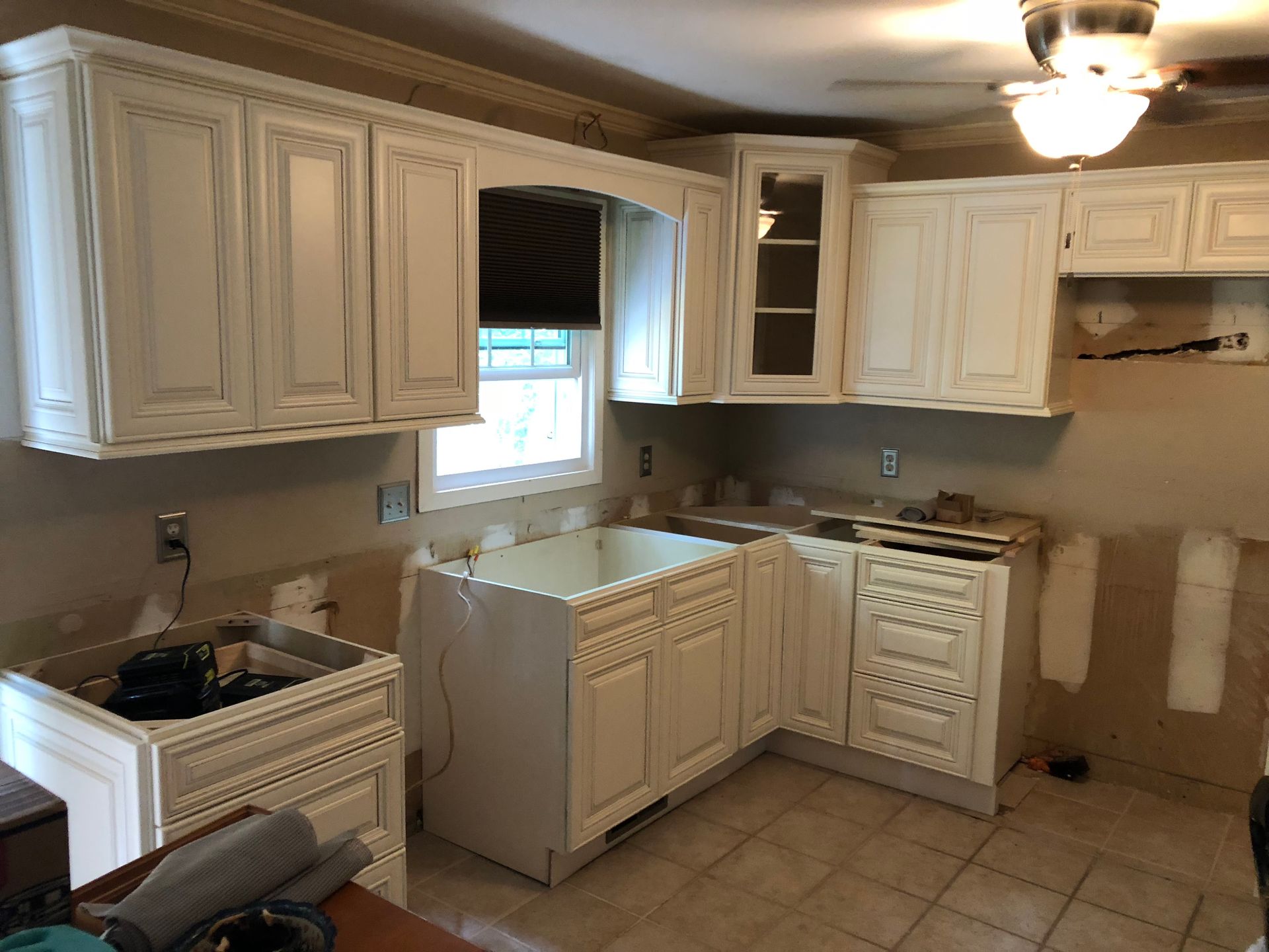 Kitchen with white cabinets under construction, window, and missing backsplash.