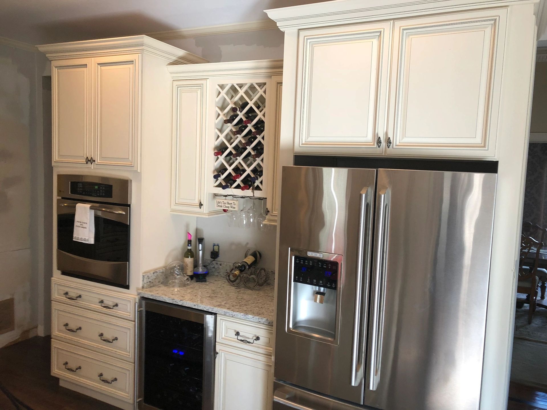 Kitchen with white cabinets, stainless steel refrigerator and oven. Wine rack, wine cooler, and countertop visible.