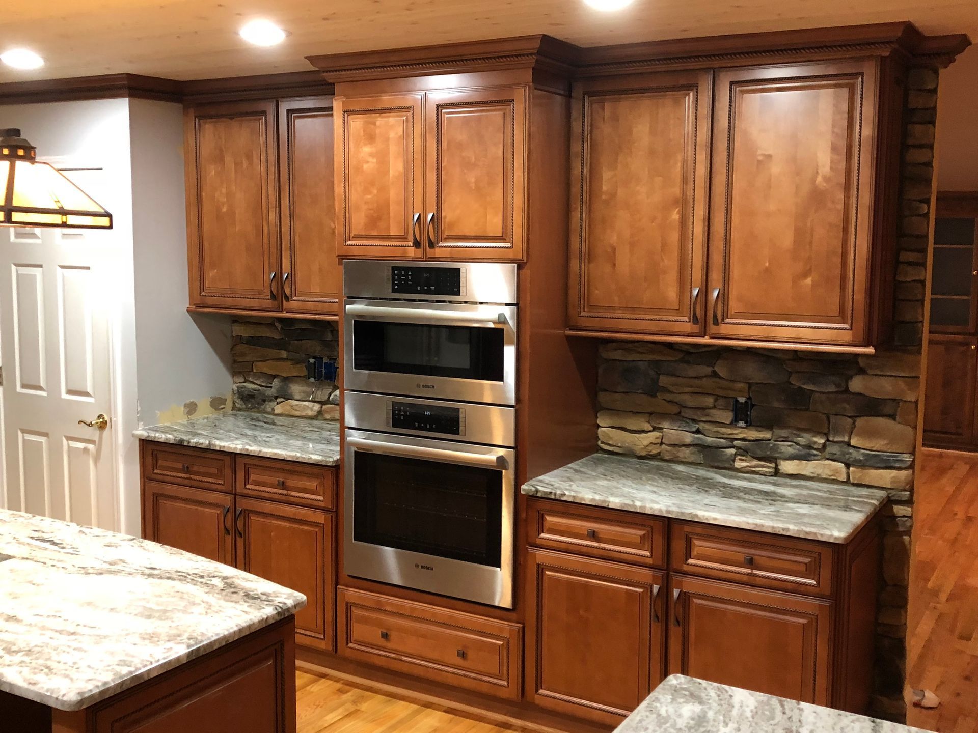 Kitchen with wood cabinets, stainless steel oven, stone backsplash, and granite countertops.