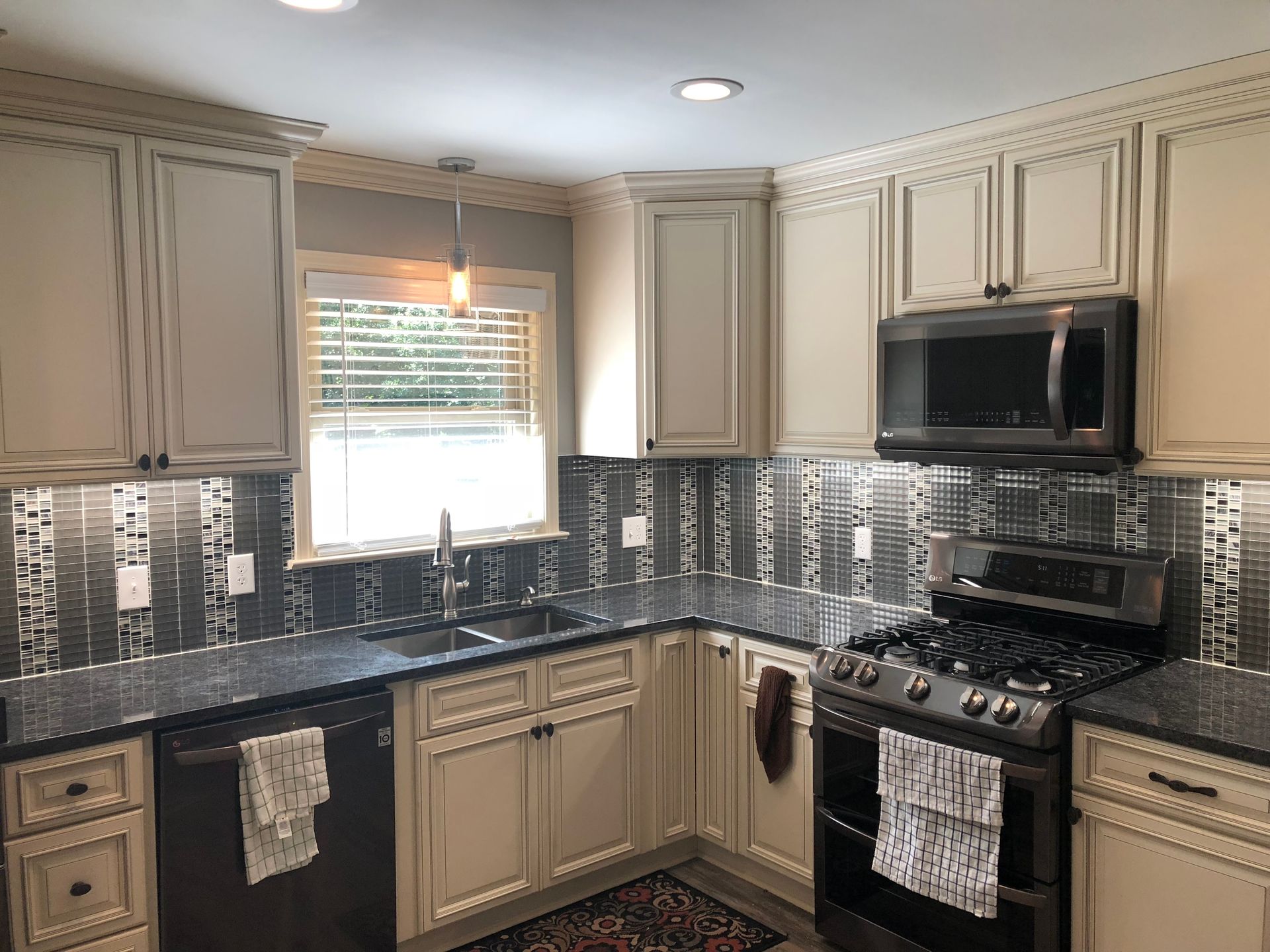 Kitchen with cream cabinets, black countertops, and a metallic tile backsplash.