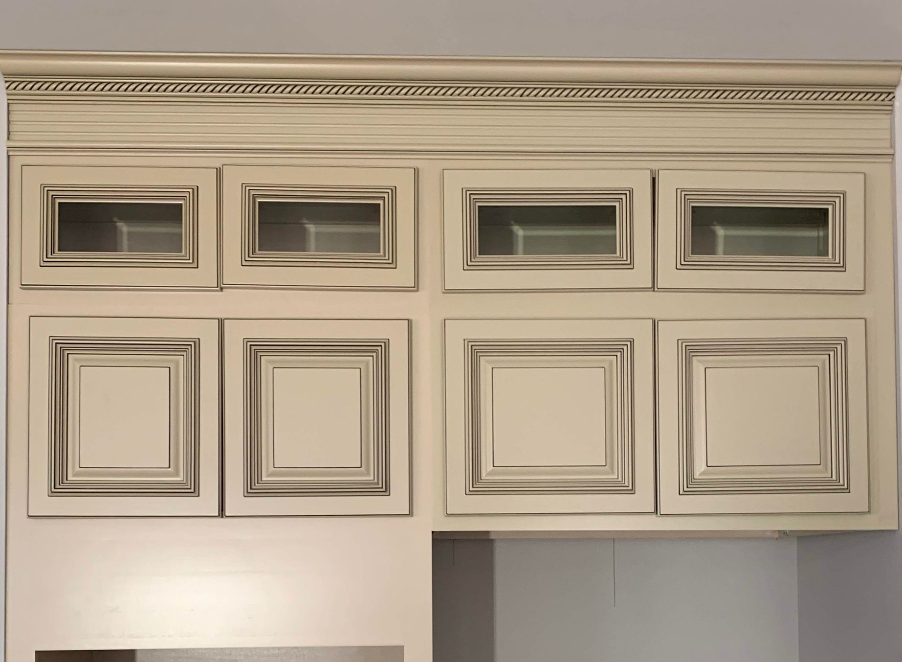 Cream-colored kitchen cabinets with glass and solid doors; decorative trim above.