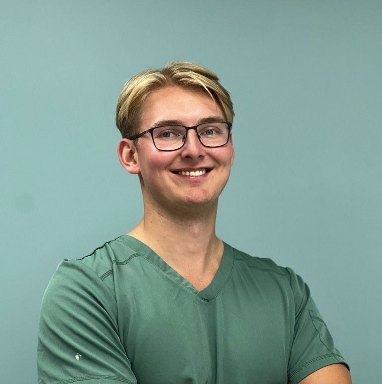 Tannlege Christian med briller og skjegg, iført blå skjorte og medisinsk maske, smiler til kameraet.