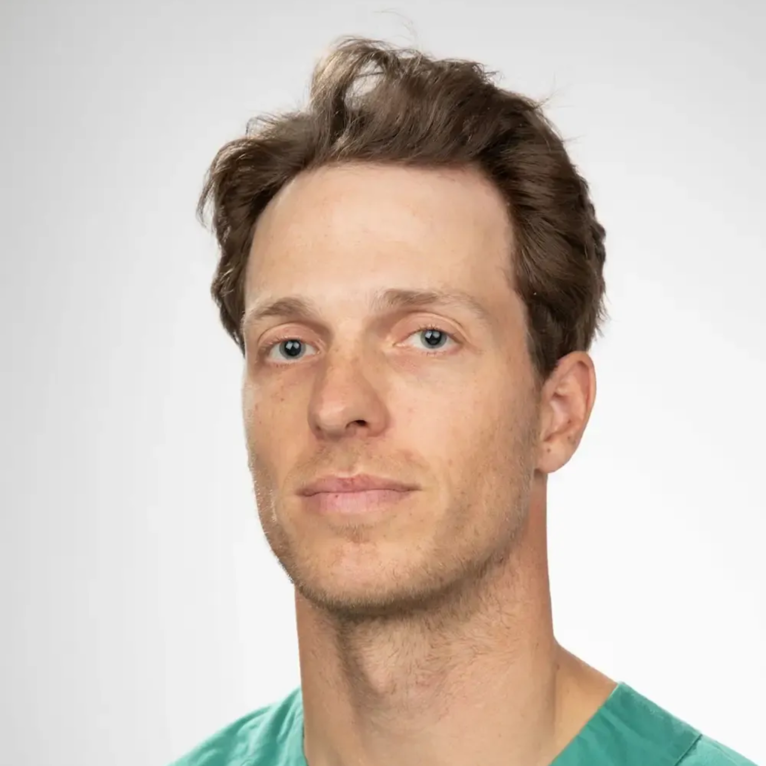 Tannlege Christian med briller og skjegg, iført blå skjorte og medisinsk maske, smiler til kameraet.