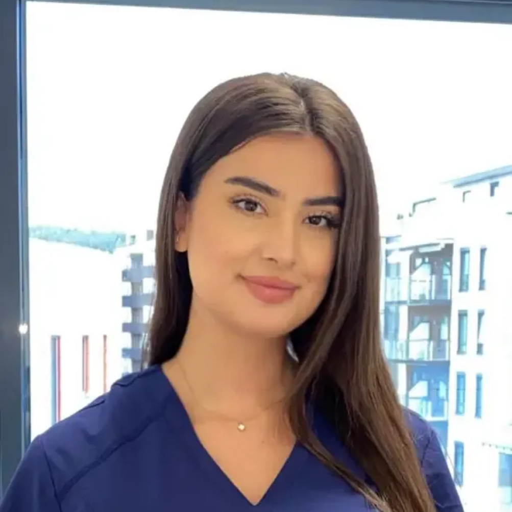 Tannlege Christian med briller og skjegg, iført blå skjorte og medisinsk maske, smiler til kameraet.