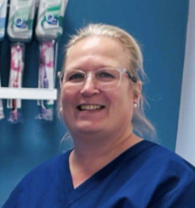 Tannlege Christian med briller og skjegg, iført blå skjorte og medisinsk maske, smiler til kameraet.