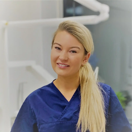 Tannlege Christian med briller og skjegg, iført blå skjorte og medisinsk maske, smiler til kameraet.