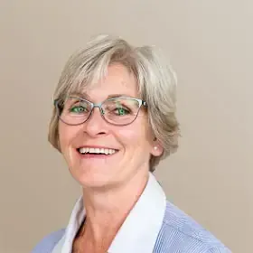 Tannlege Christian med briller og skjegg, iført blå skjorte og medisinsk maske, smiler til kameraet.