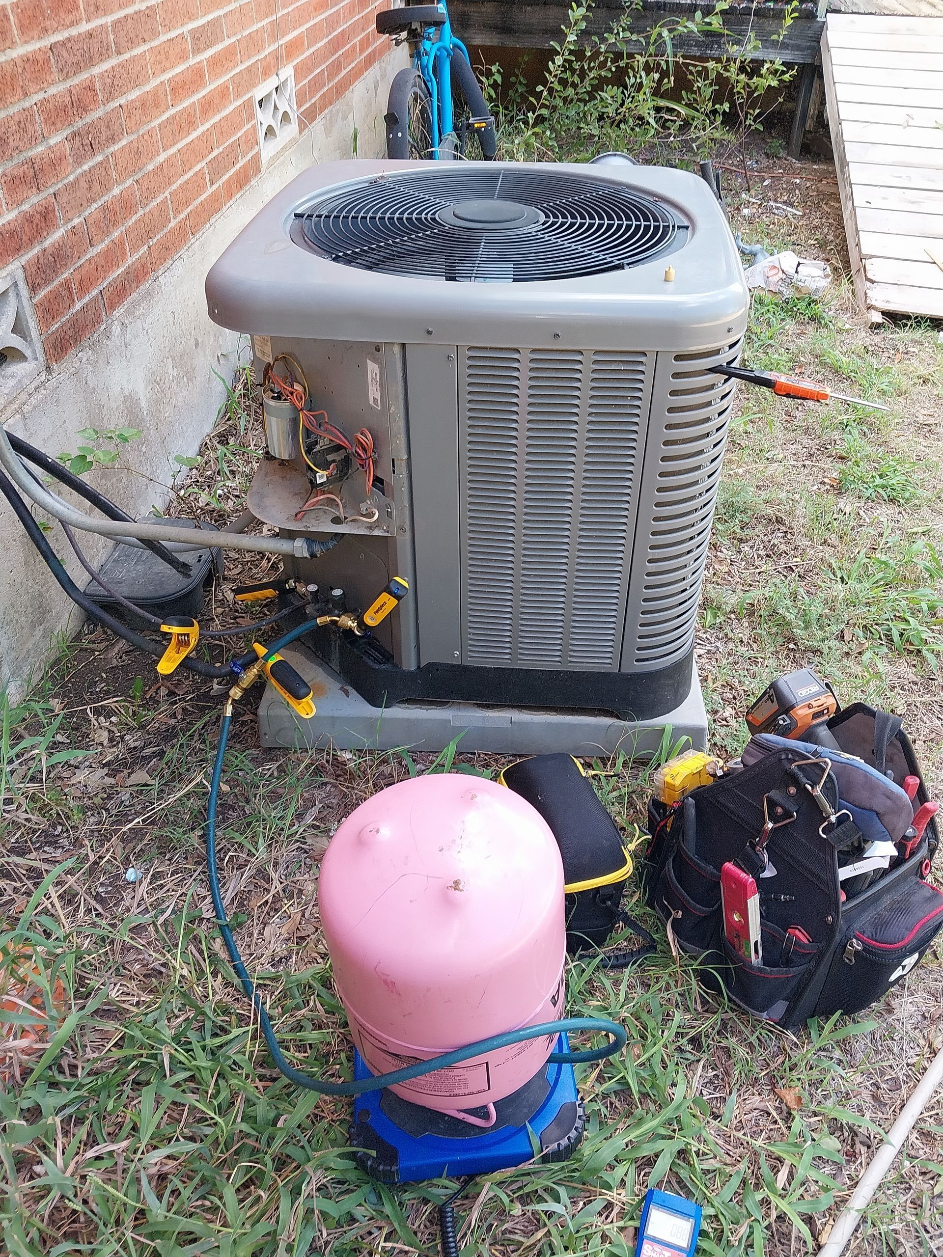 An air conditioner is being repaired in the backyard of a house.