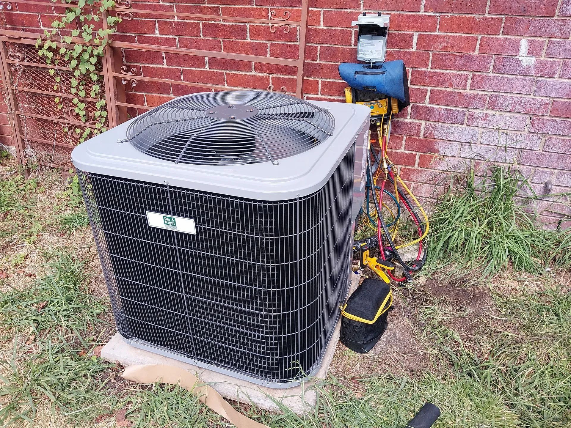 AC unit outside a brick building, being serviced with gauges and tools.