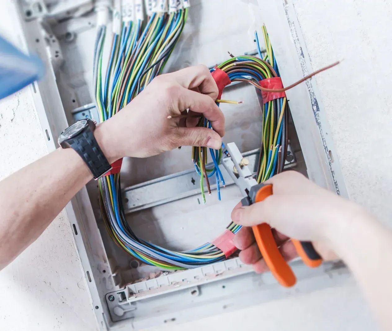 Hands wiring a circuit panel with multicolored cables and orange wire strippers