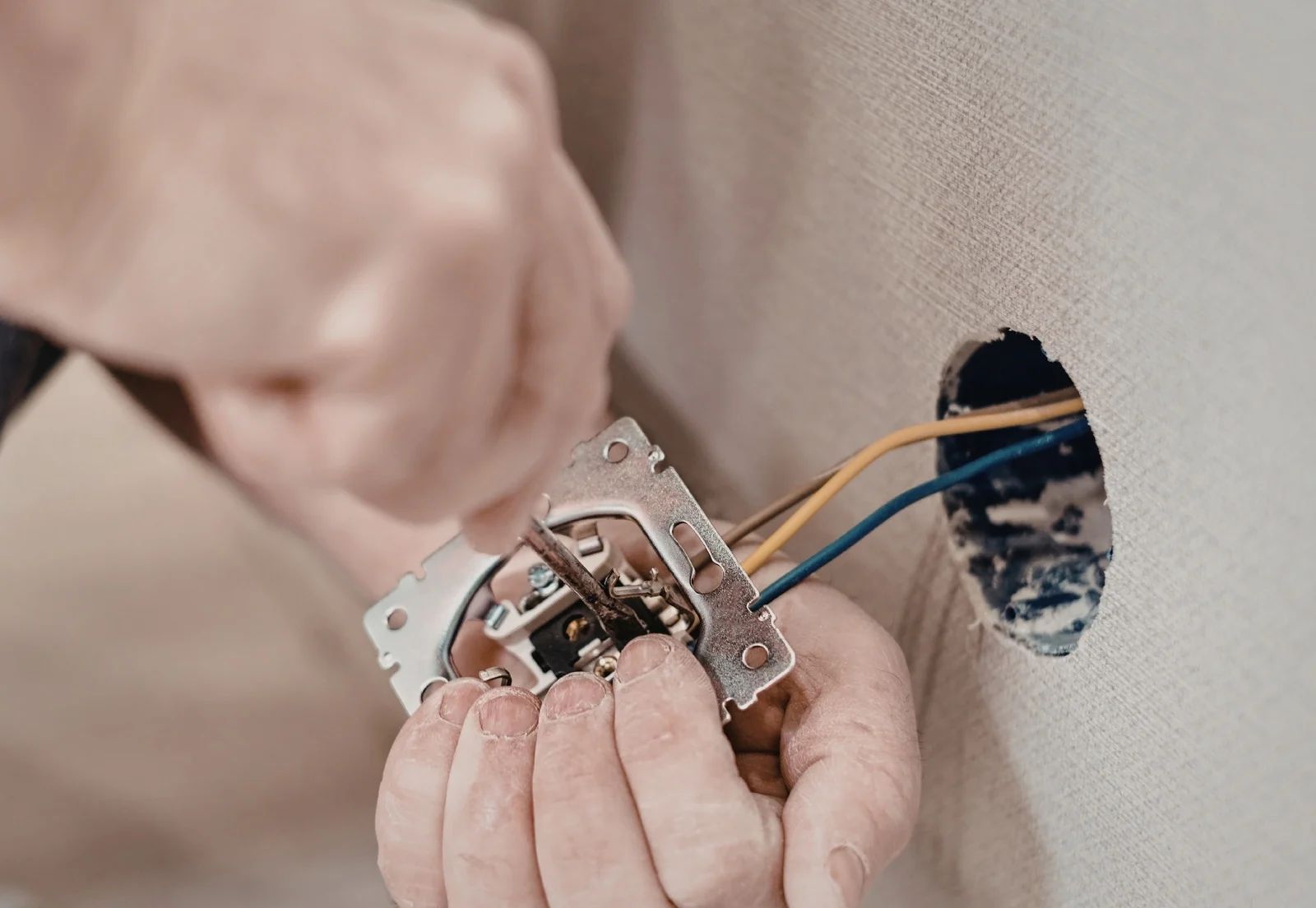 A person installs or repairs an electrical switch, connecting wires inside a wall socket opening.