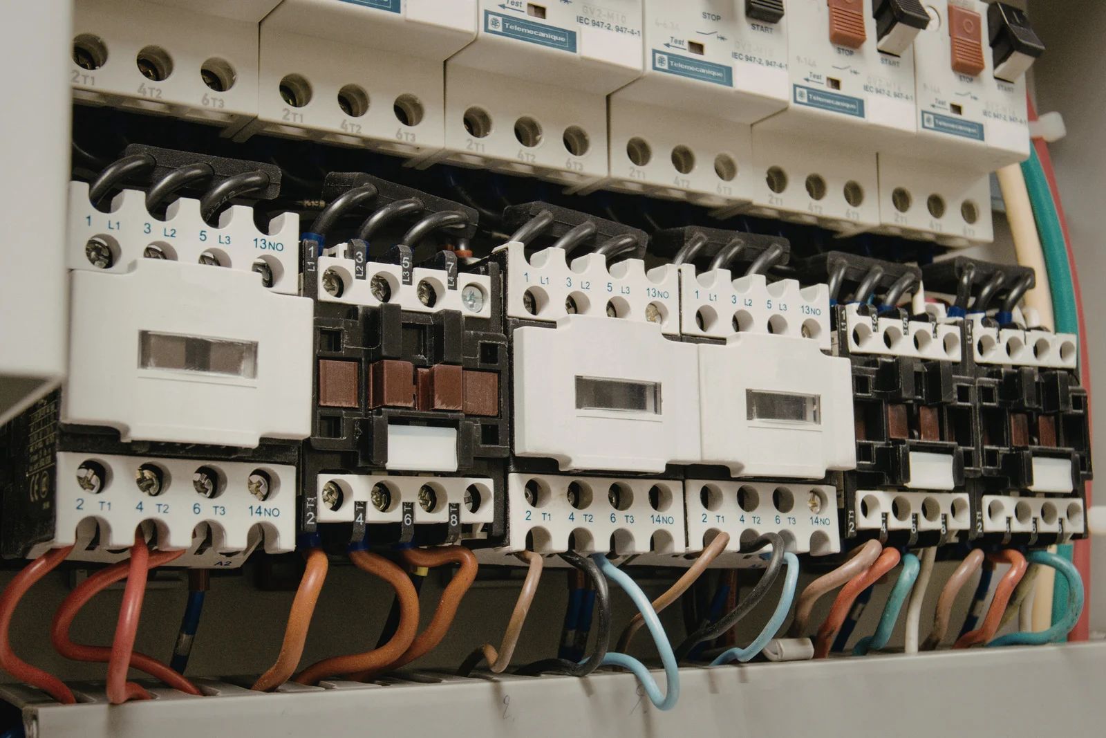 Electrical components with white casings, screw terminals, and connected colored wires arranged in a control cabinet.