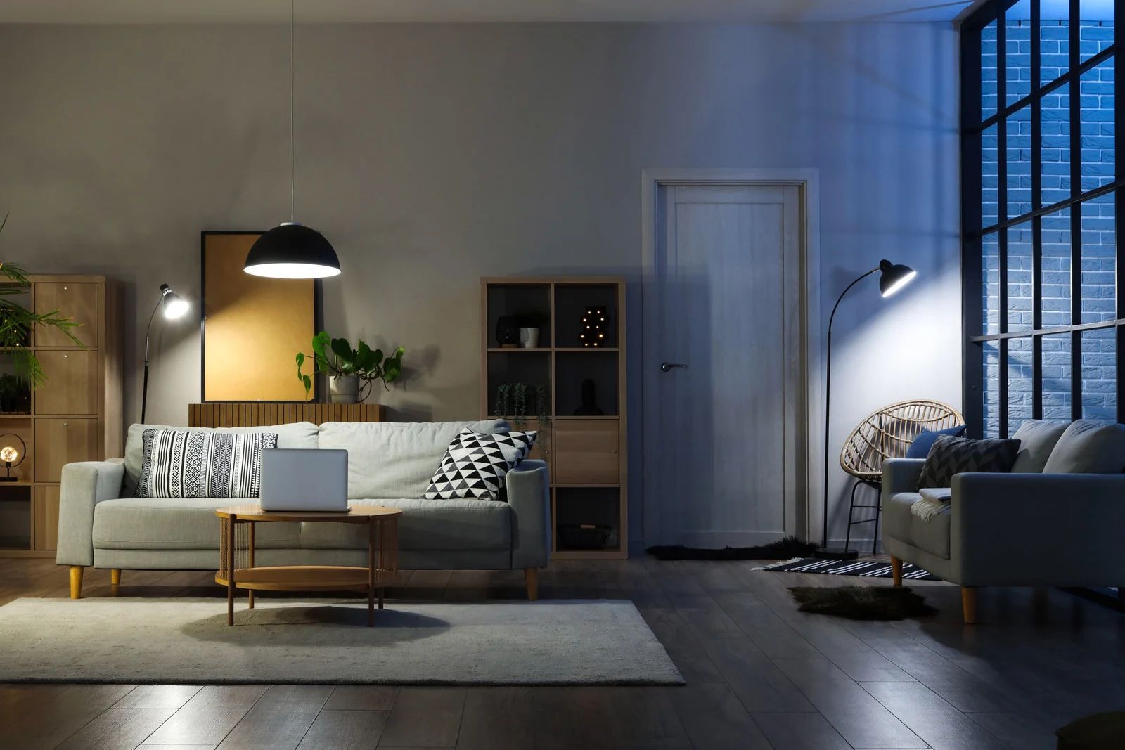 Cozy living room at night with two sofas, floor lamps, wooden furniture, and a large window with a city view.