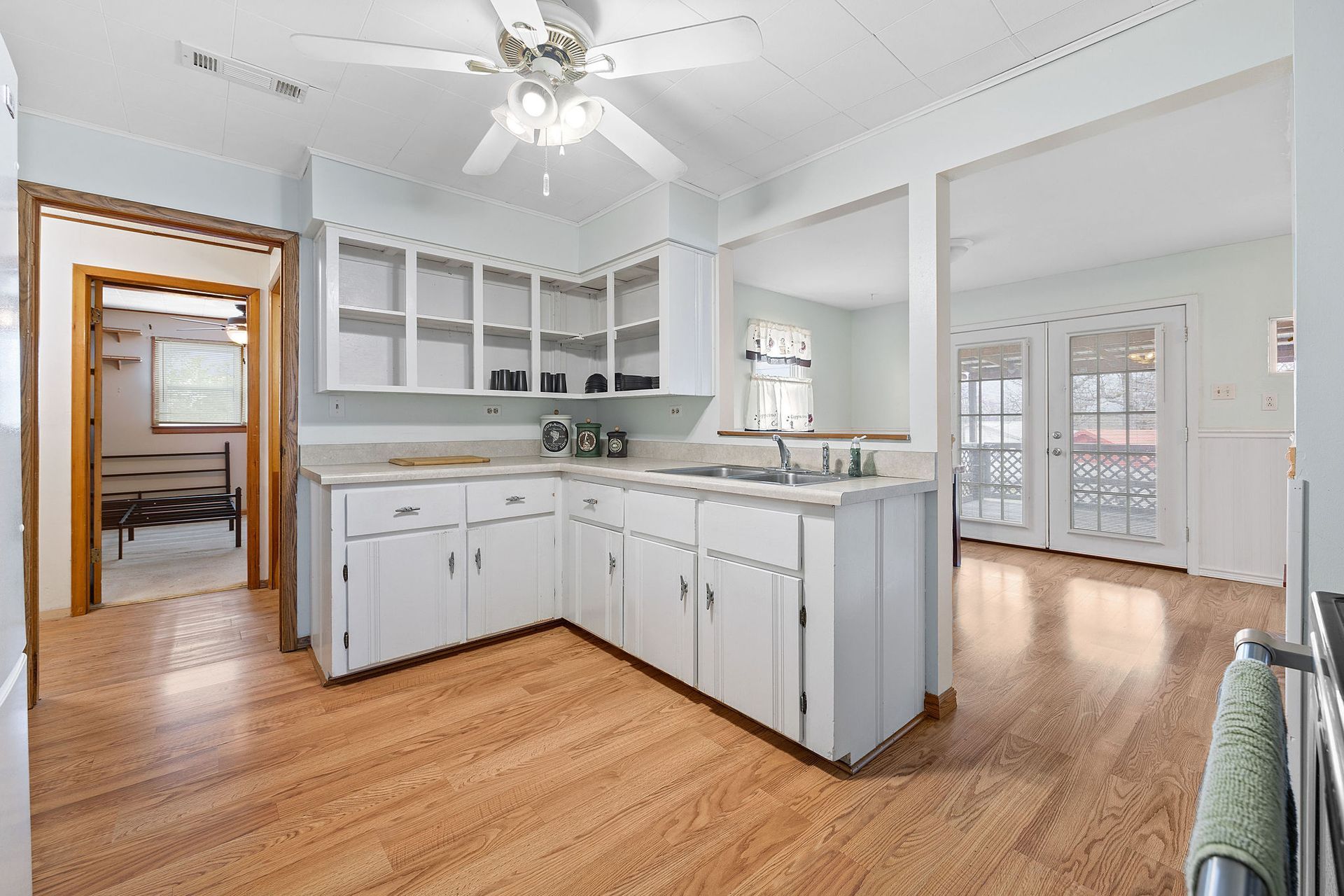 A kitchen with white cabinets and hardwood floors and a ceiling fan.