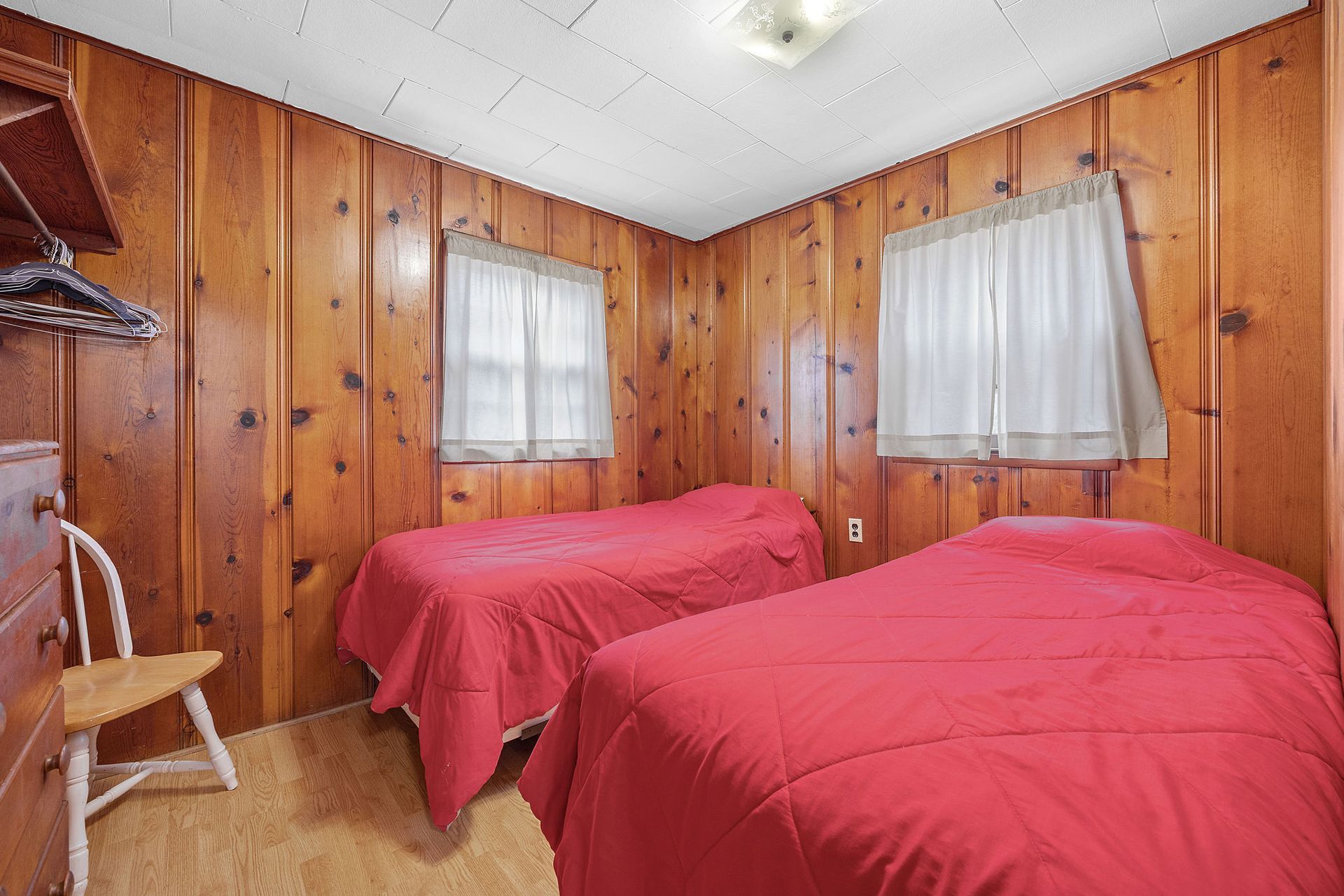 A bedroom with two beds and wood paneled walls.