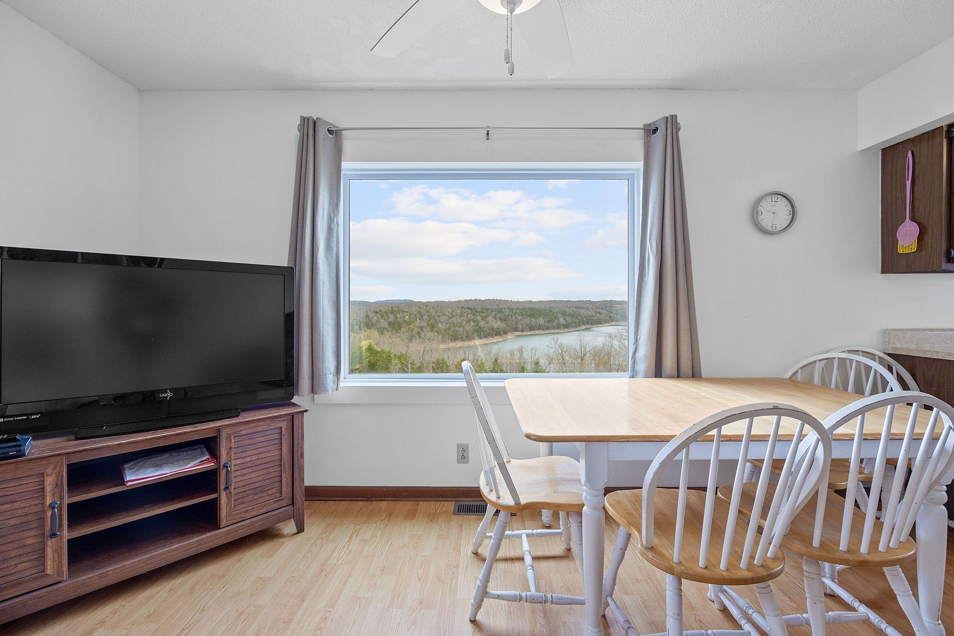 A living room with a table , chairs , television and a large window.