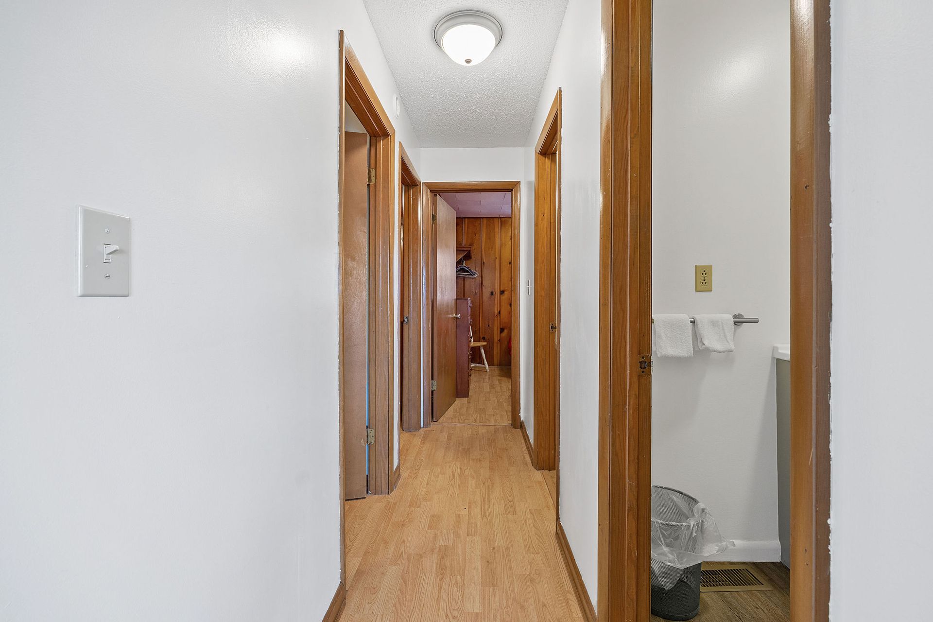 A hallway in a house with wooden floors and white walls leading to a bathroom.