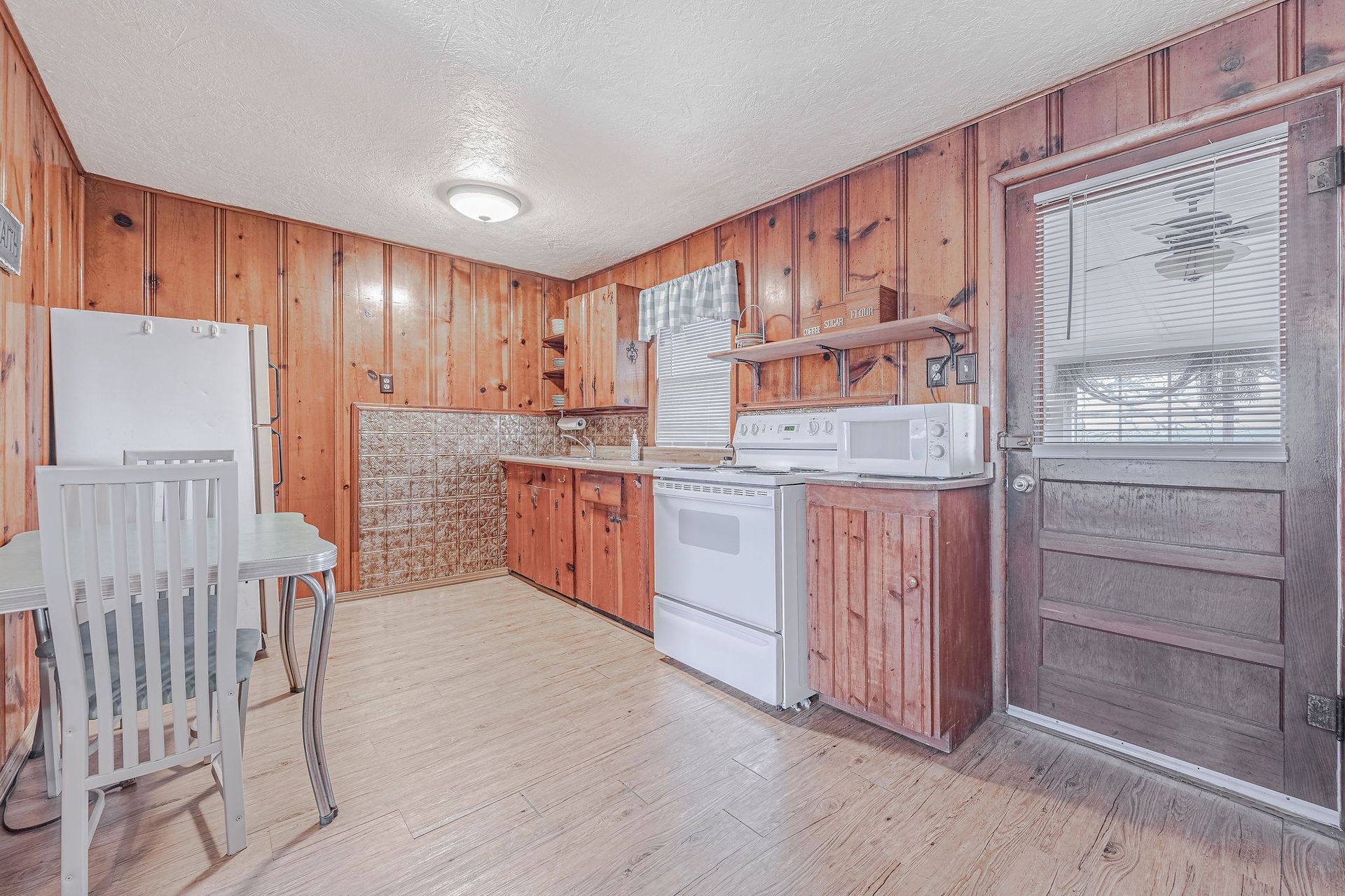 A kitchen with wooden cabinets , white appliances , a table and chairs.