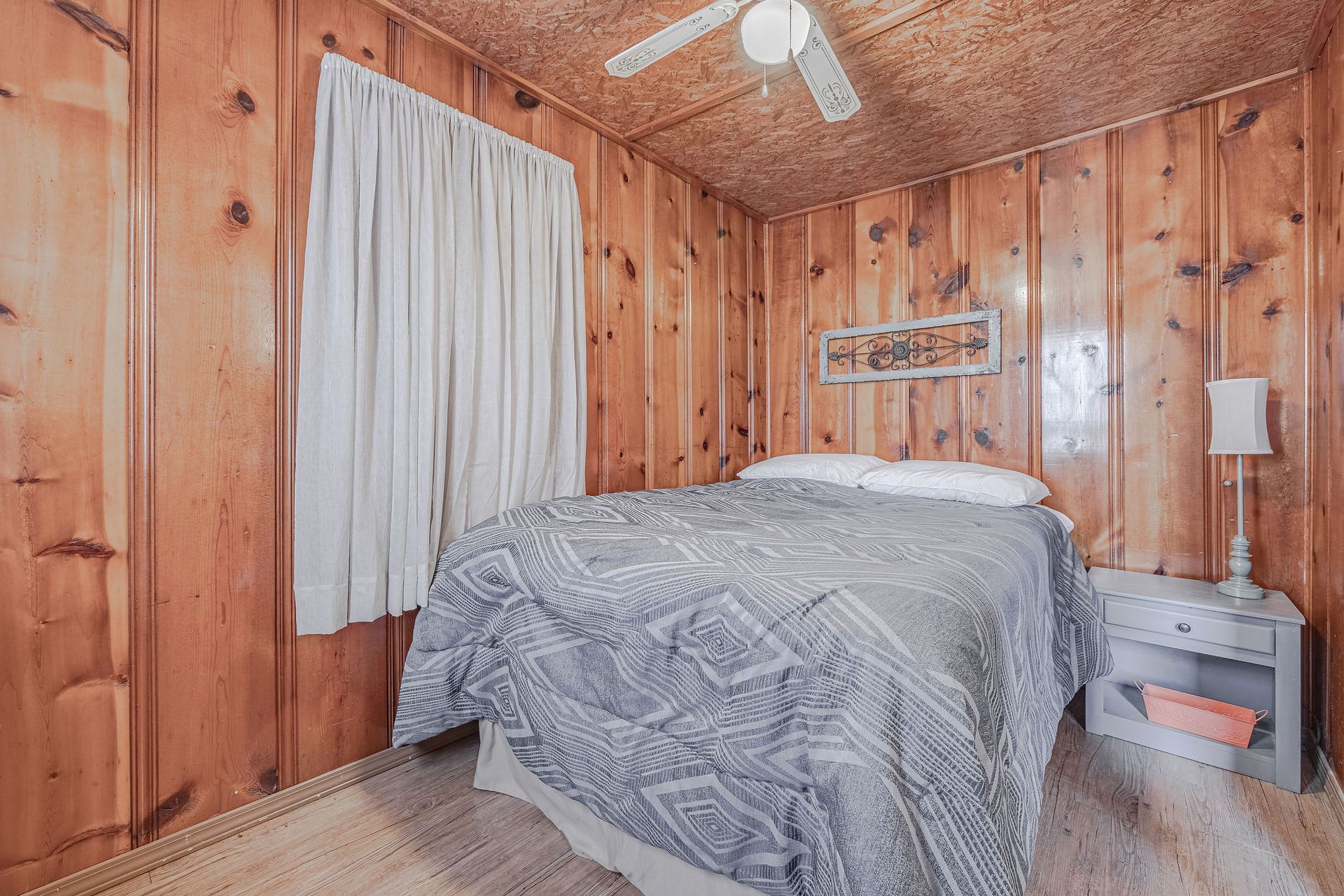 A bedroom with a bed , nightstand , lamp and ceiling fan.