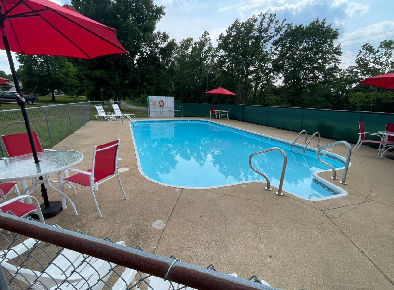 A large swimming pool surrounded by chairs , tables and umbrellas.