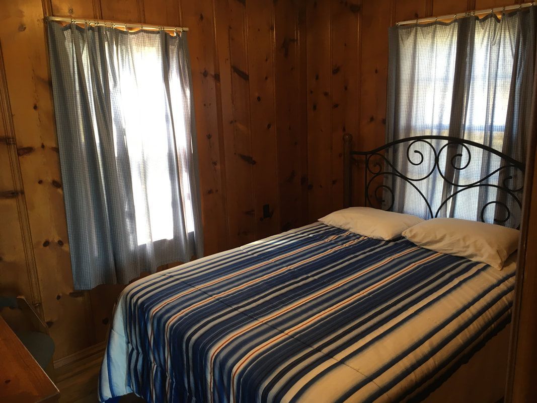 A bedroom with a bed and two windows with blue curtains.