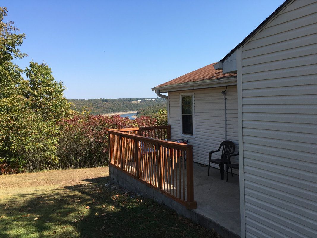 A white house with a wooden deck and a view of a lake.