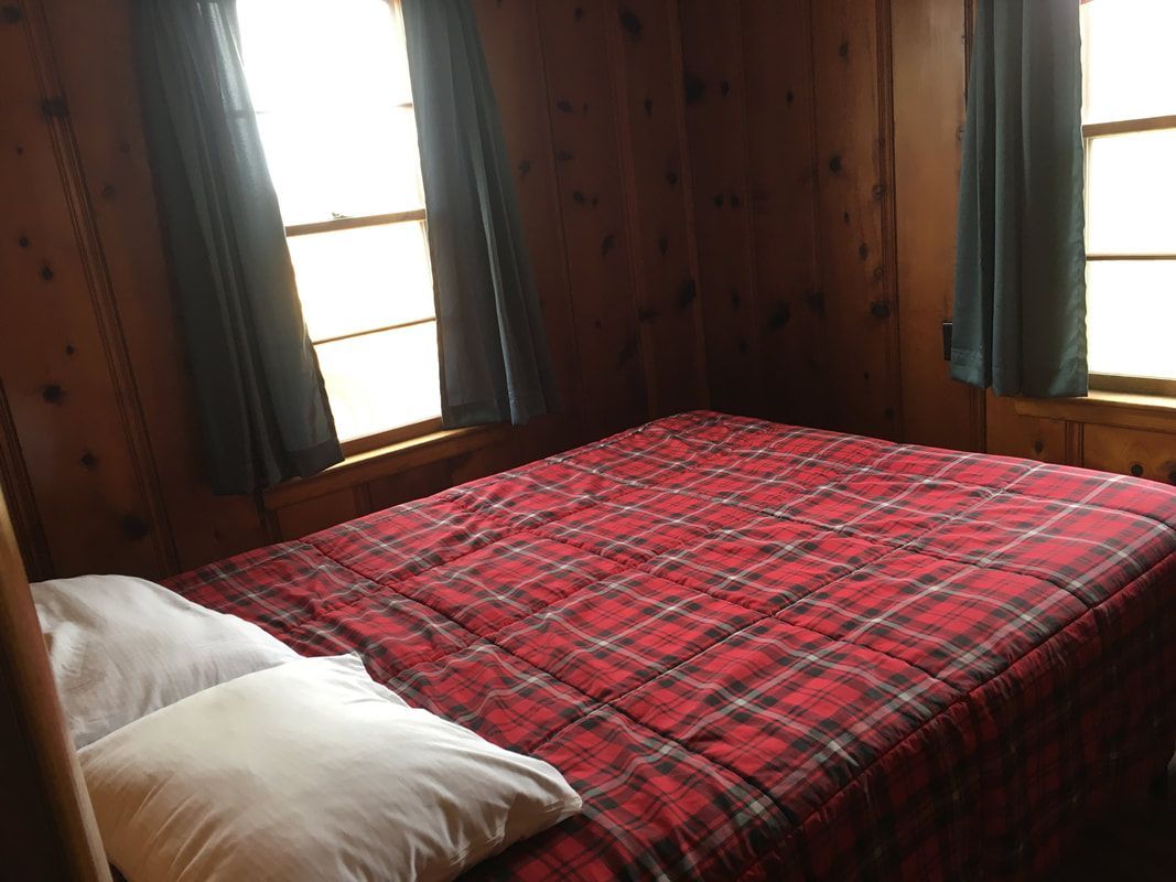 A bedroom with a bed and two windows with a red plaid blanket.