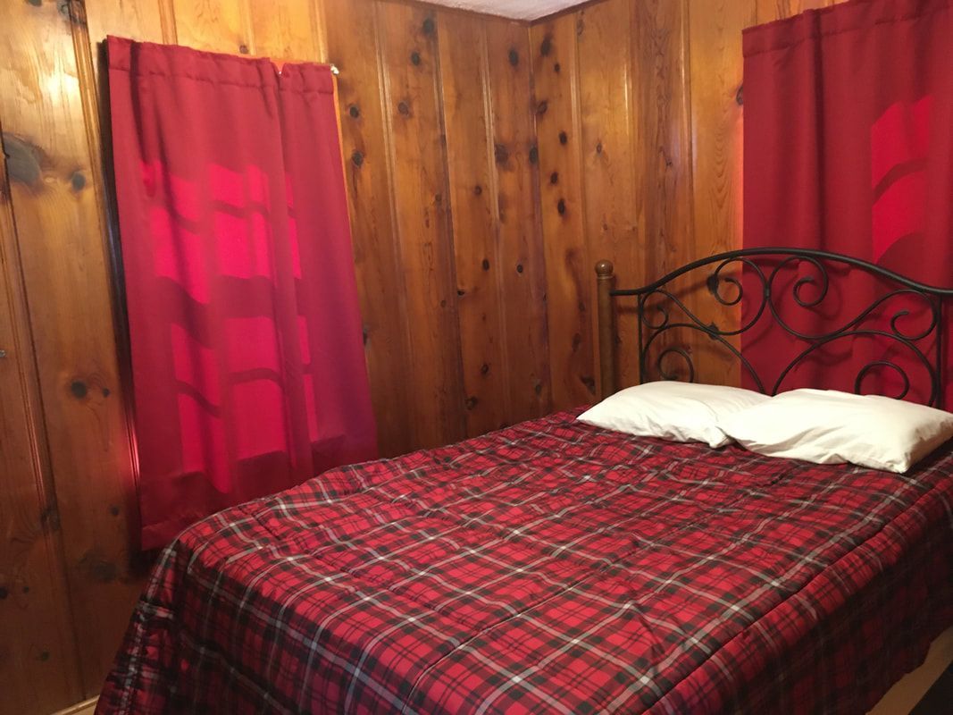 A bedroom with a bed and two windows with red curtains.