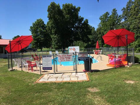 A swimming pool with red umbrellas and chairs around it.