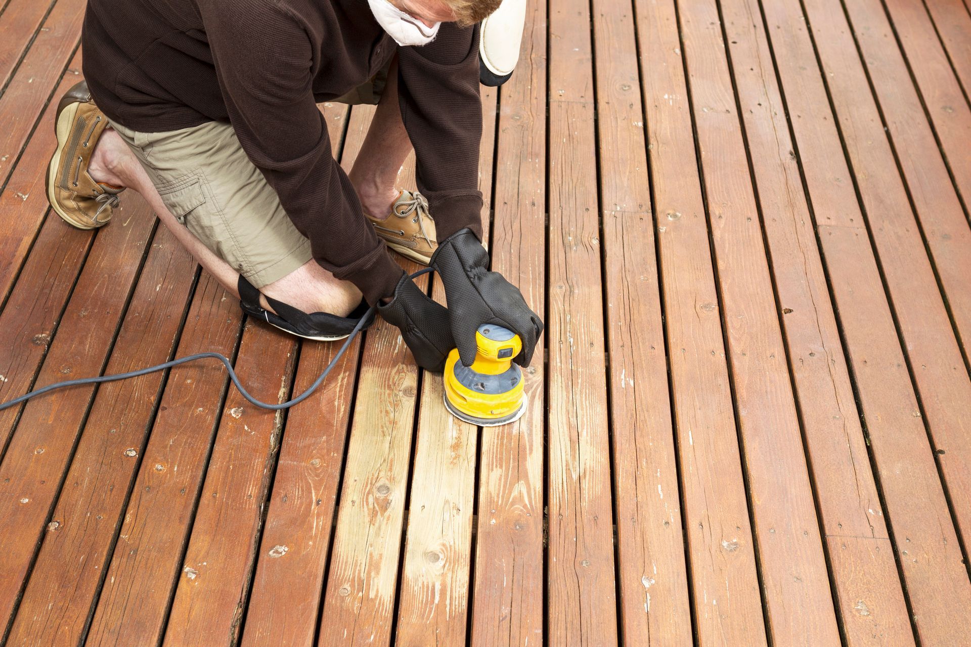 An experienced worker repairs a wooden deck, sanding down rough surfaces and replacing damaged boards to ensure safety and structural integrity.