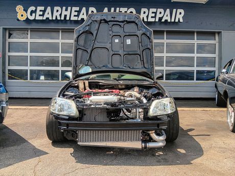 Black car with hood open, showing engine modifications, in front of 