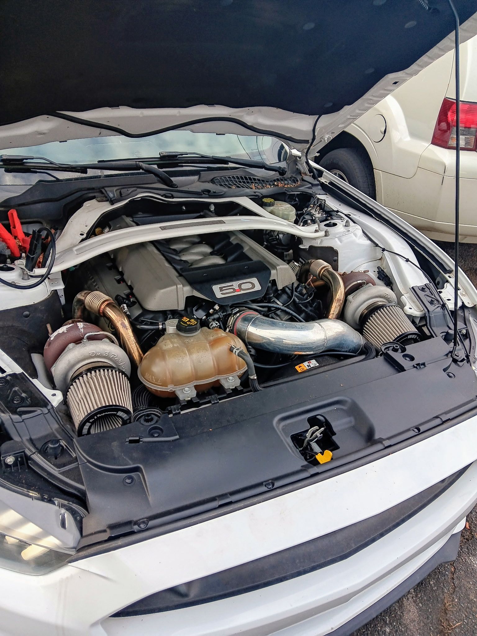 White Mustang with open hood, twin turbochargers visible.