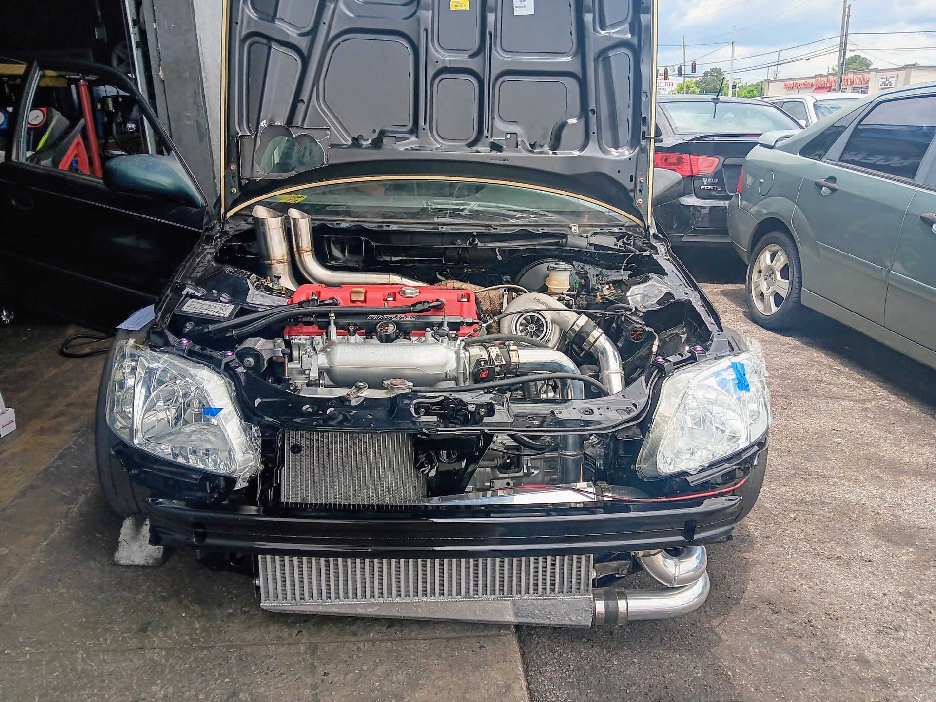 Black car with open hood, engine visible. Front intercooler, turbo setup, in an outdoor setting.