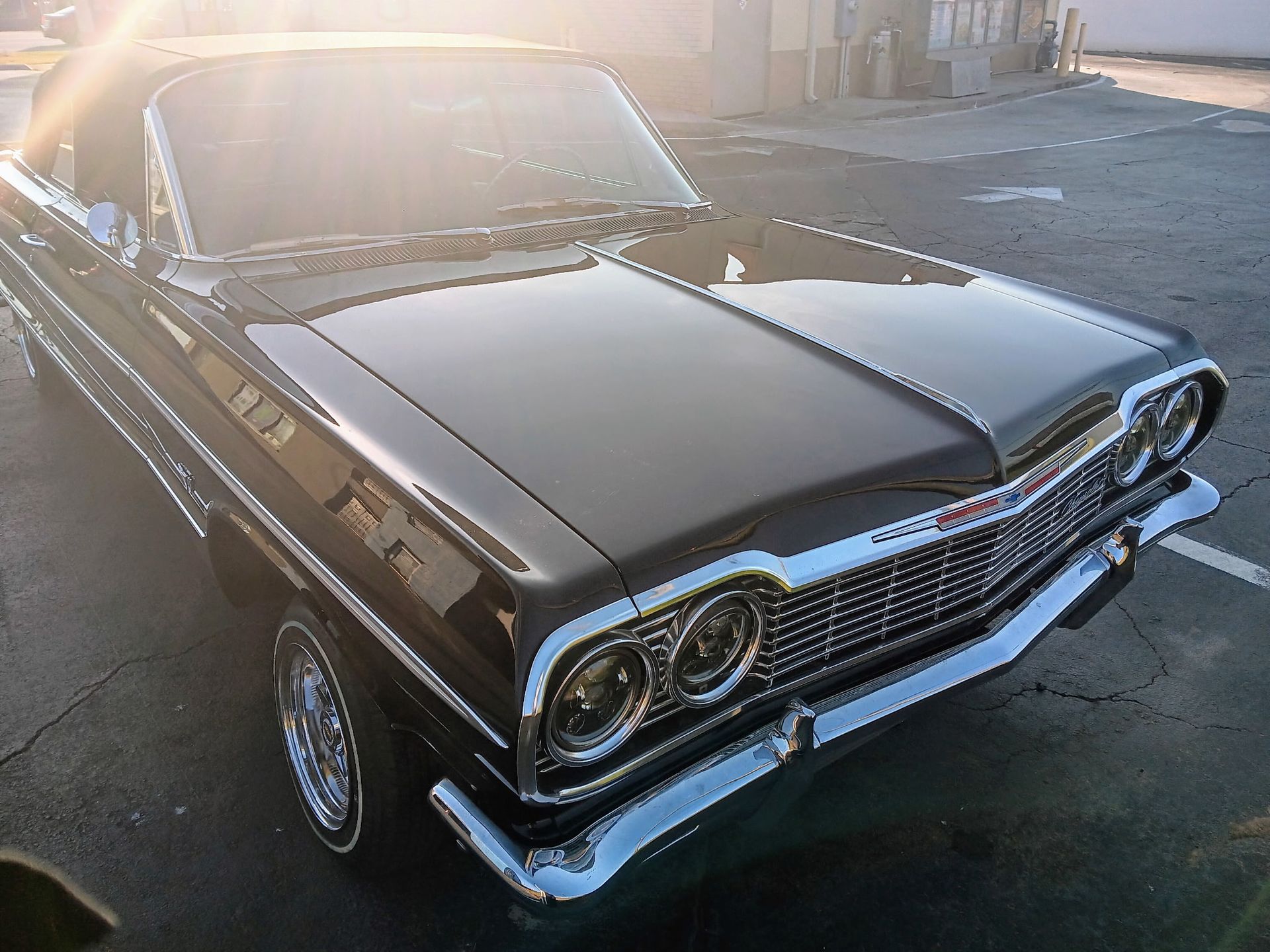 Black classic car parked on asphalt, chrome details, bright sunlight.