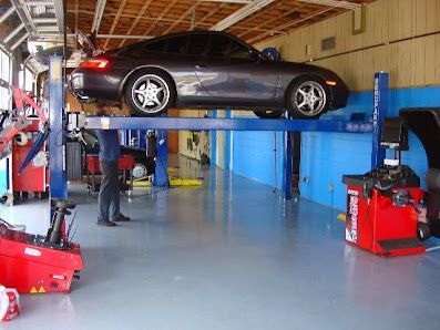 Car on a blue lift inside a garage. A person is working on the car.