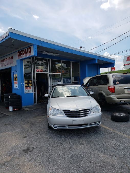 Silver car parked in front of a blue auto repair shop; tires visible. Sunny day.