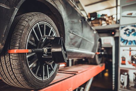 Car wheel being aligned on a lift in a garage. Black car, red lift, measuring tools attached.