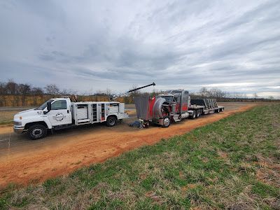 A tow truck is driving down a dirt road next to a field.