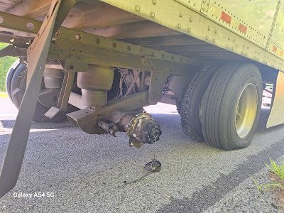 A semi truck with a broken axle is sitting on the side of the road.