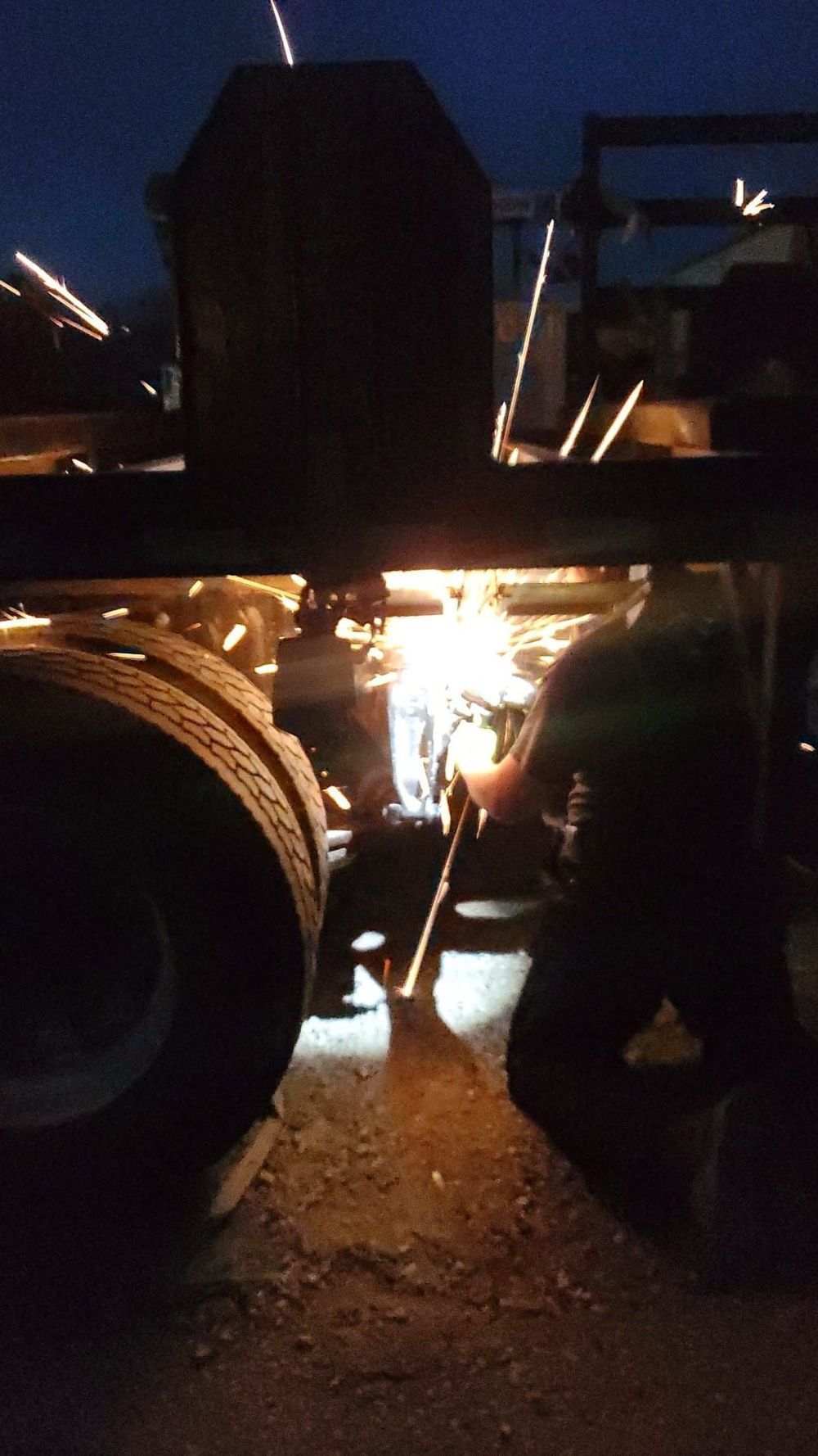 A truck is being worked on at night with a welding machine
