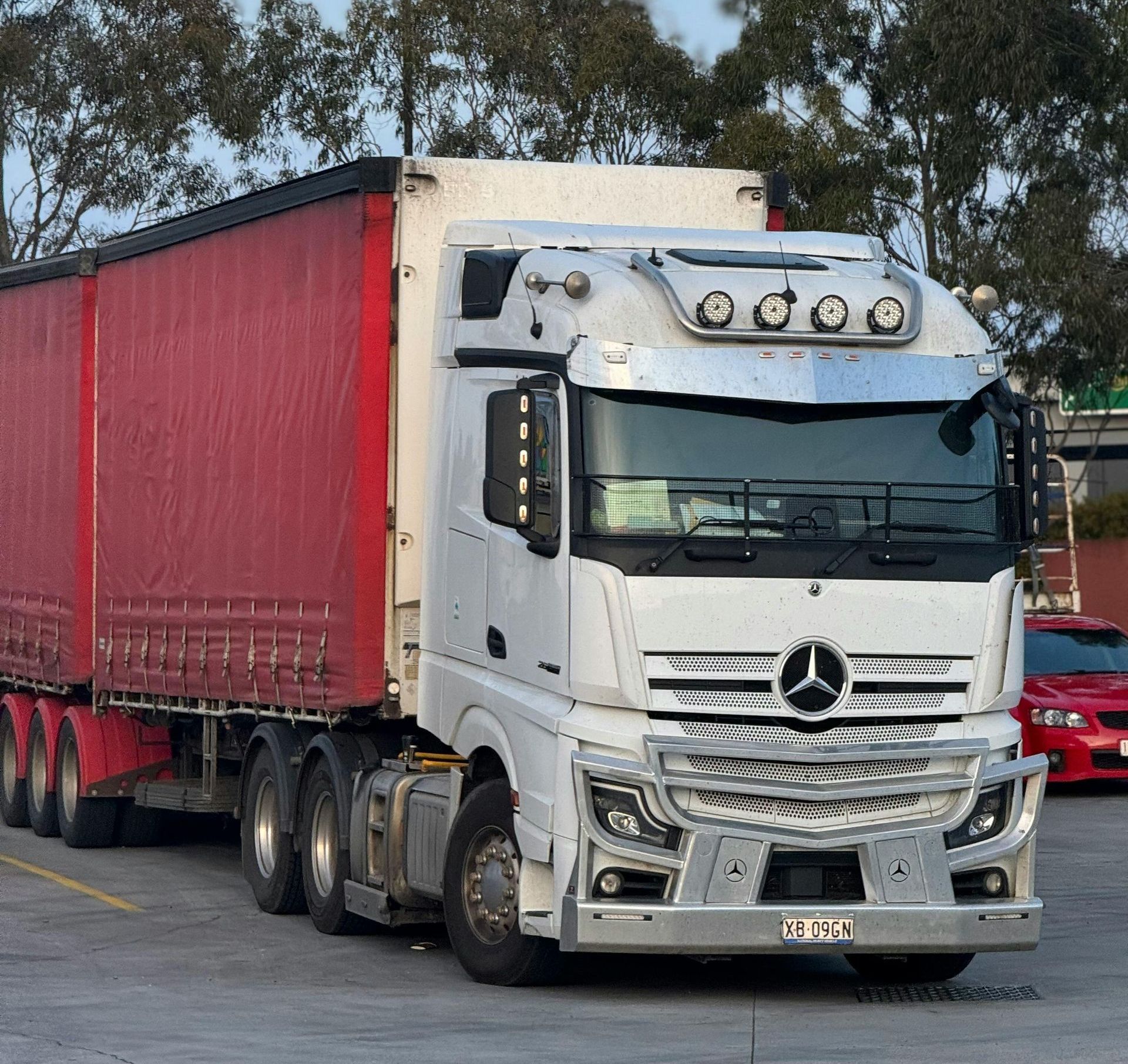 A white mercedes truck with a red trailer is parked in a parking lot