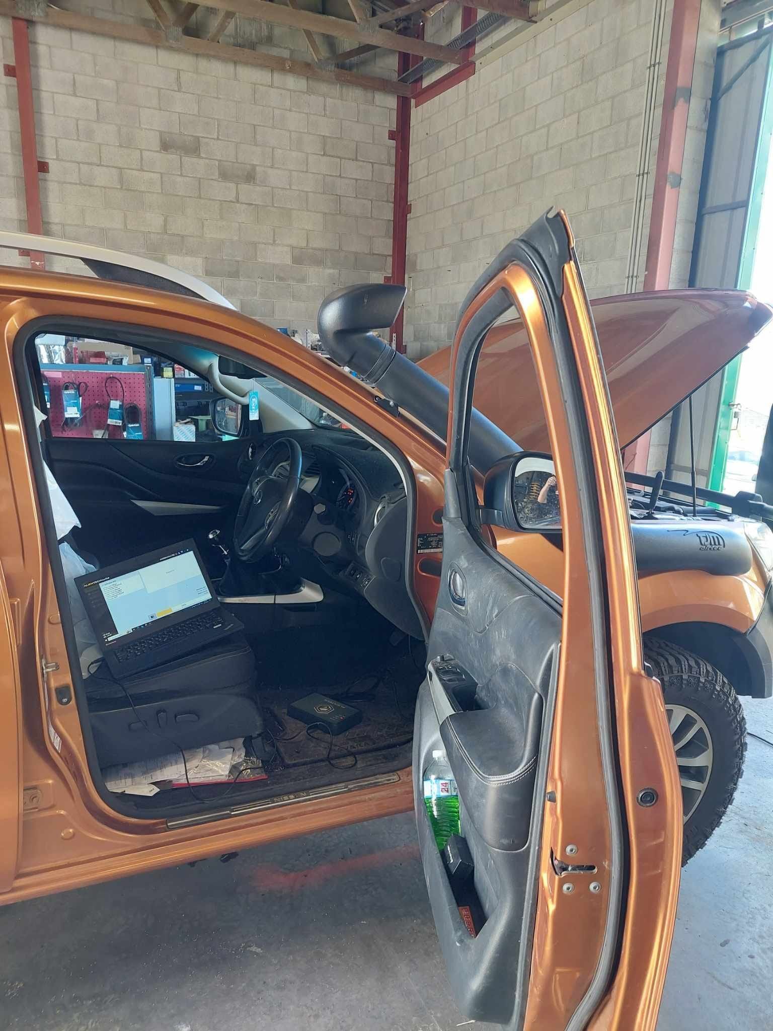 Orange pickup truck with open doors inside a garage; hood open, snorkel.