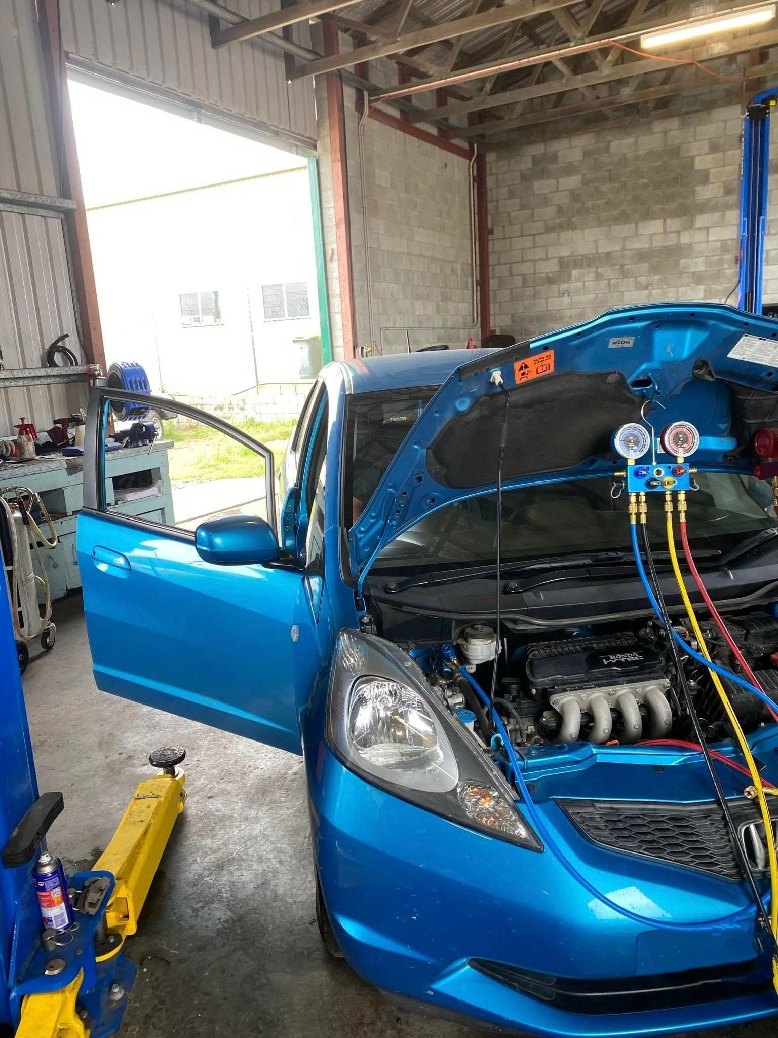 Blue car with open hood and door in a garage, hooked up to diagnostic equipment.