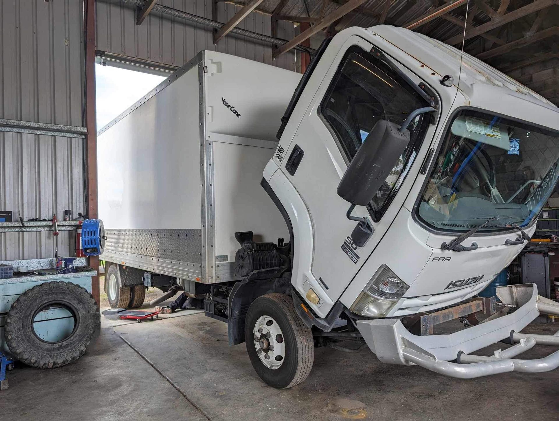White Isuzu box truck with its cab tilted up in a workshop.