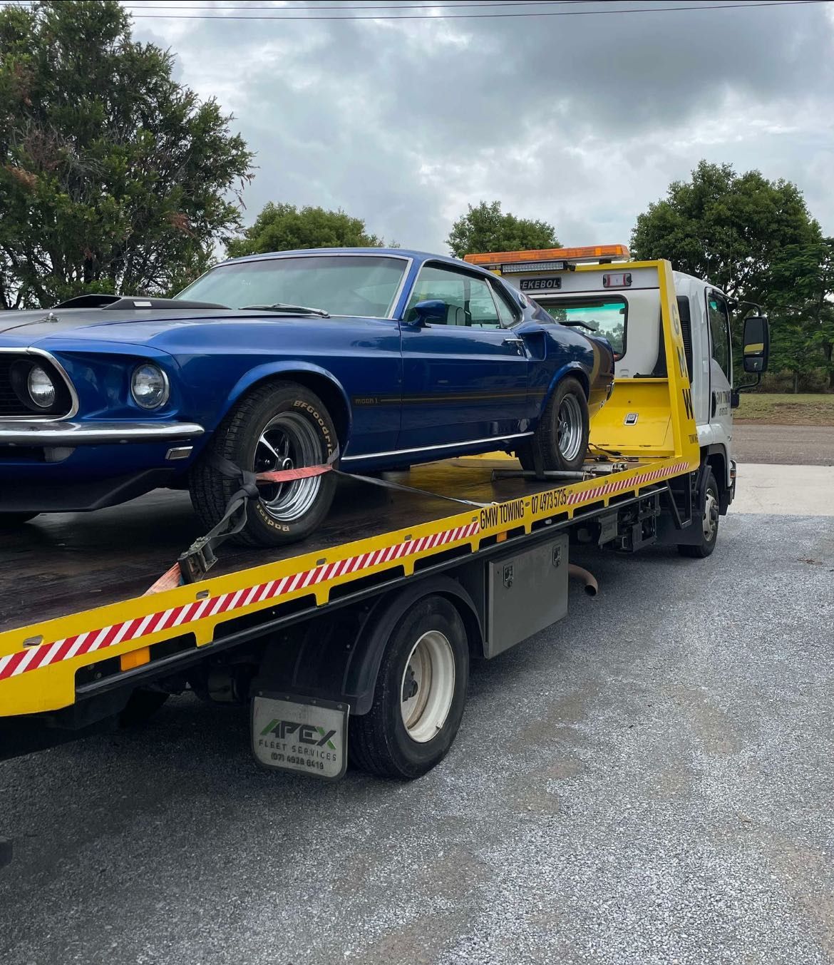 Blue classic Ford Mustang loaded on a yellow flatbed tow truck.