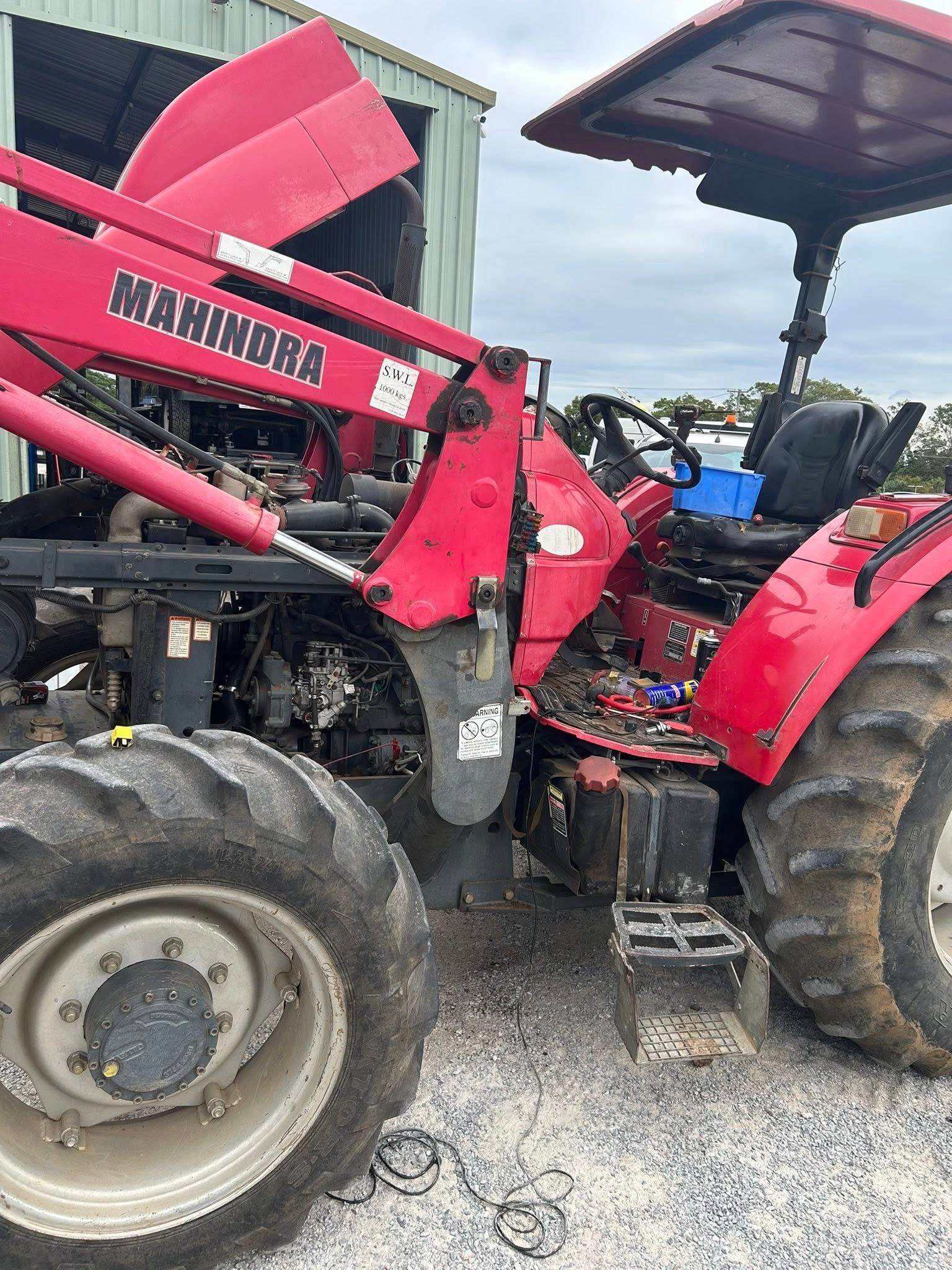 Red Mahindra tractor with front-end loader; parked outdoors with hood open.